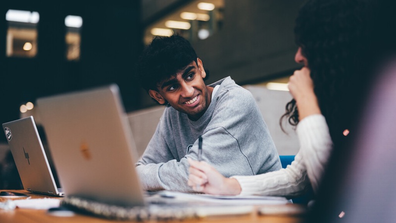 Two students with their laptops sitting at a desk