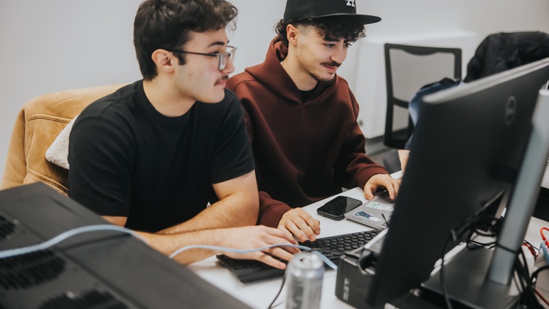 Two students with their laptops sitting at a desk