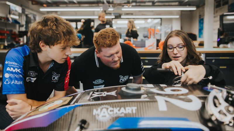 Three students leaning on motorsport car