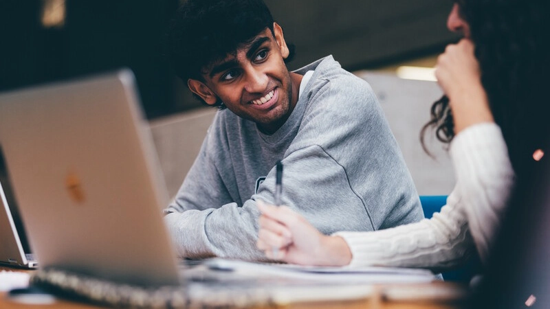 Smiling male student looking towards a female student while they study