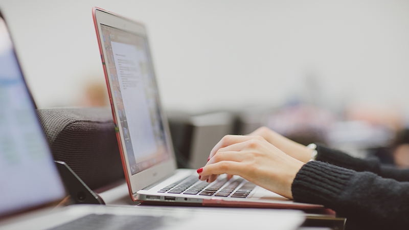 female student's hands typing on laptop