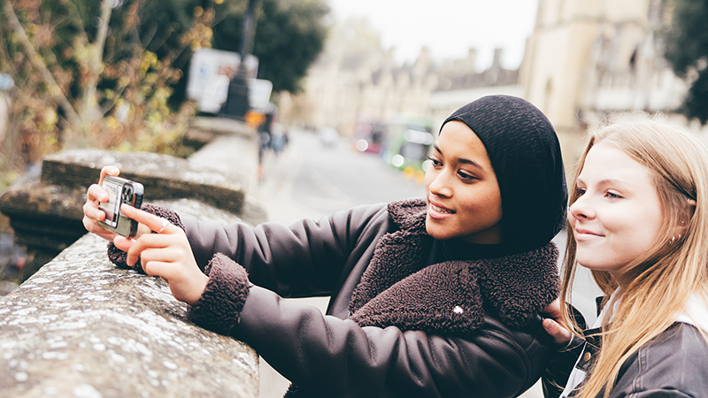 Two female students taking photos on Magdalen Bridge, Oxford