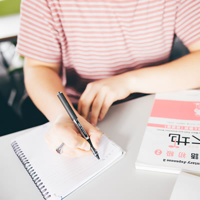 A student writing on a desk with Japanese text book