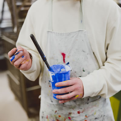 Student holding a blue paint pot with paint on their hands