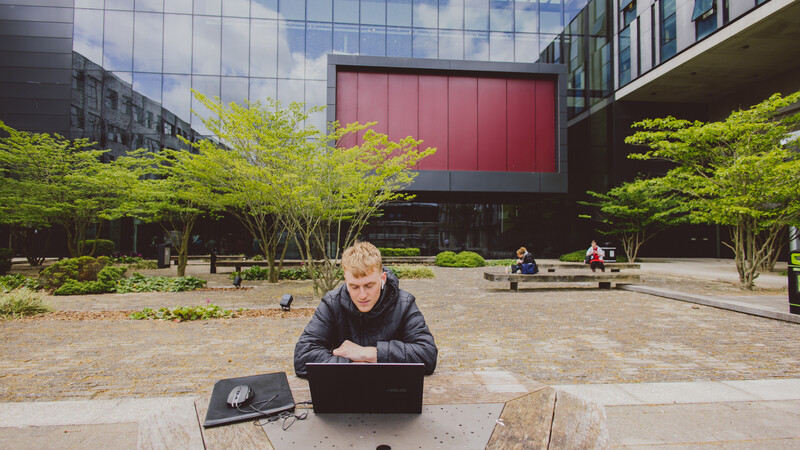 Male student sitting outside John Henry Brookes building studying