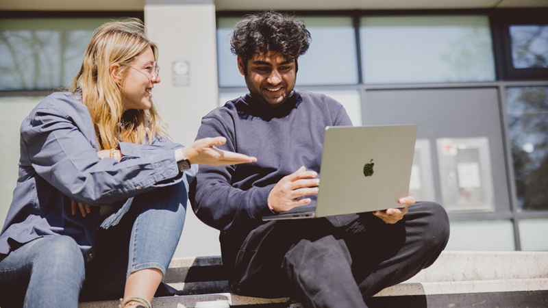 Two Philosophy, Politics and Economics (PPE) students outside discussing a paper on a laptop
