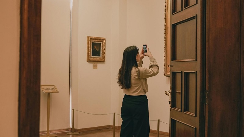 Person in an art gallery capturing a photo of an artwork