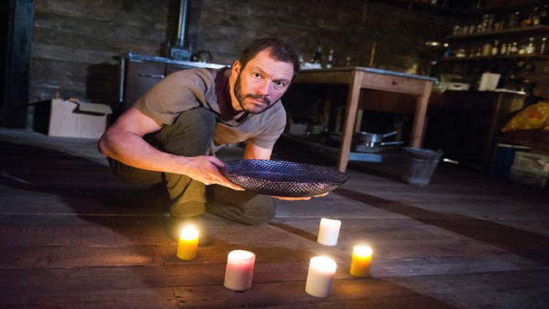 Actor Dominic West kneeling on stage next to some candles