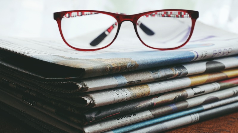 red frames glasses sitting on a pile of folded newspapers