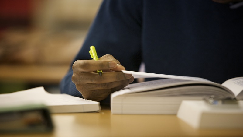 Student's hand holding a pen and turning the page of a book