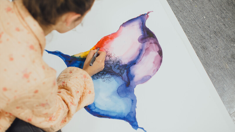 A person painting an abstract colourful painting on a white canvas