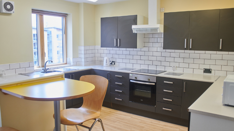 Modern kitchen with dark cupboards and white wall tiles. Small two seater breakfast table to the bottom left corner of the photo.