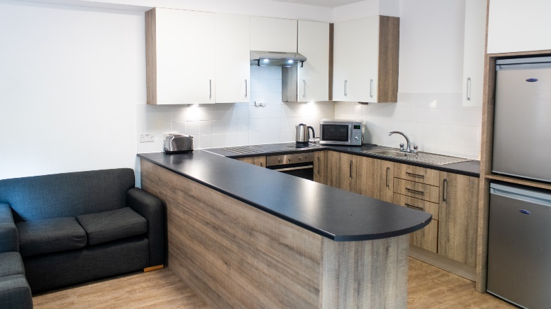 Modern kitchen with white and wood effect and black counter tops. Black leather sofa to the left.