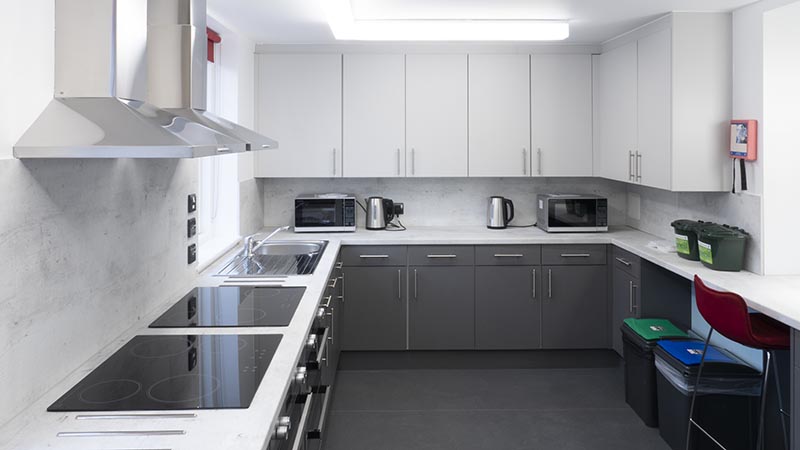 Modern grey and white kitchen with two hobs, two fans, two microwaves and two kettles.