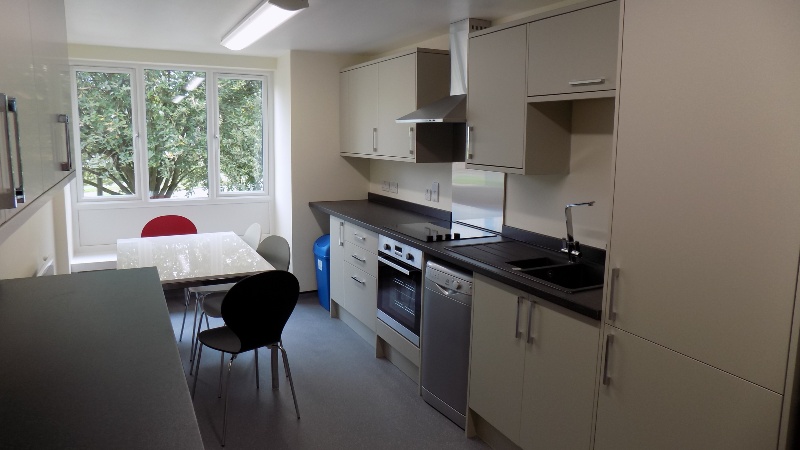 Cream coloured kitchen with large windows, black counter tops and a white dining table.