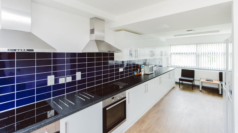 Large kitchen with all cabinets down one wall, blue tiles. white cabinets with black counter spaces.