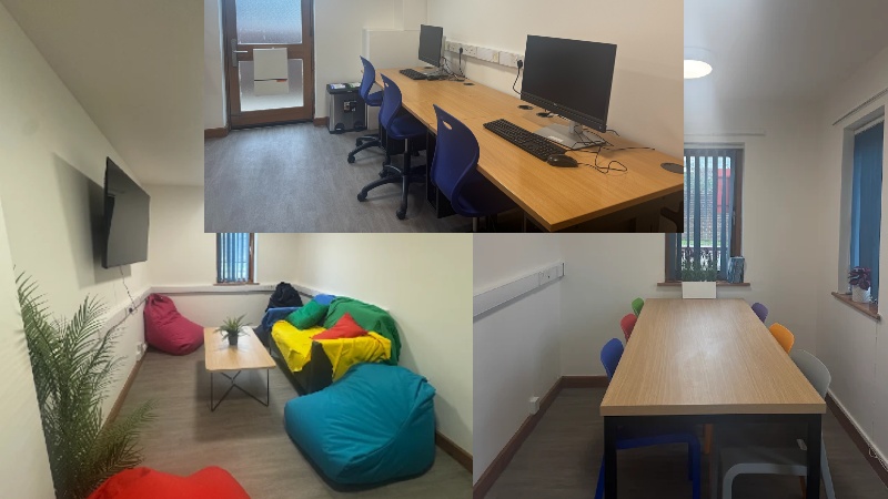 Room with sofa, bean bags, coffee table and TV on the wall. Also a large table with coloured chairs and a small computer area with 2 PCs.