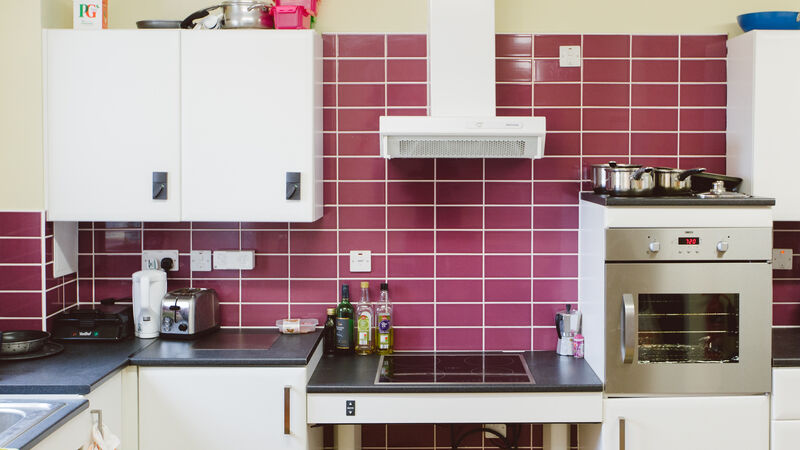 White kitchen, black counter tops, purple wall tills and height adjustable hob.