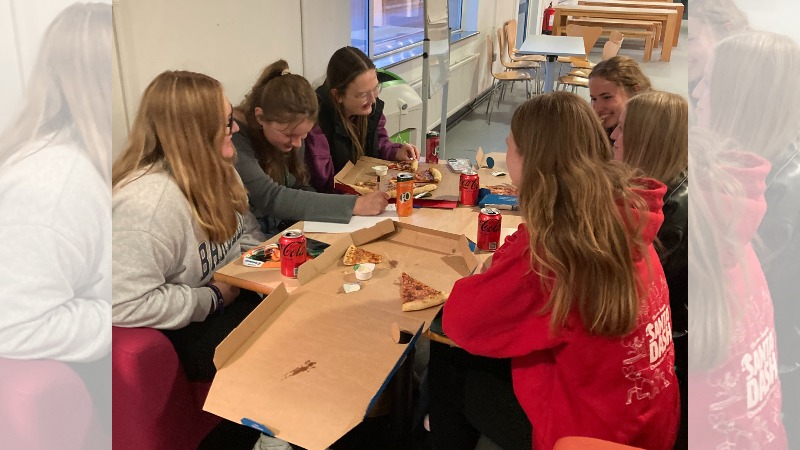 Students sat round a table with pizza and soft drink cans