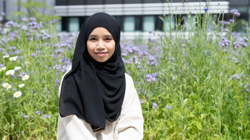 Nurfathun Mohd Sabri pictured sitting in front of wildflowers on the Oxford Brookes Headington campus.