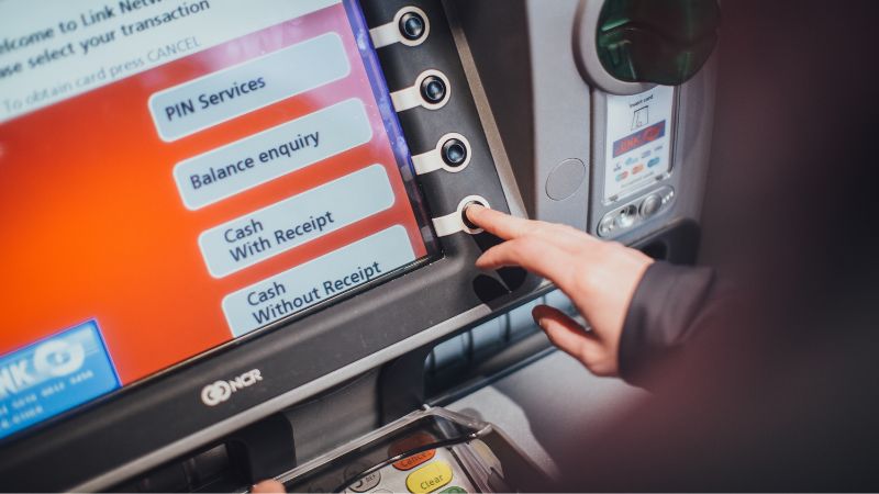 Close-up of a someone's hand pressing a button on a cash machine with screen visible