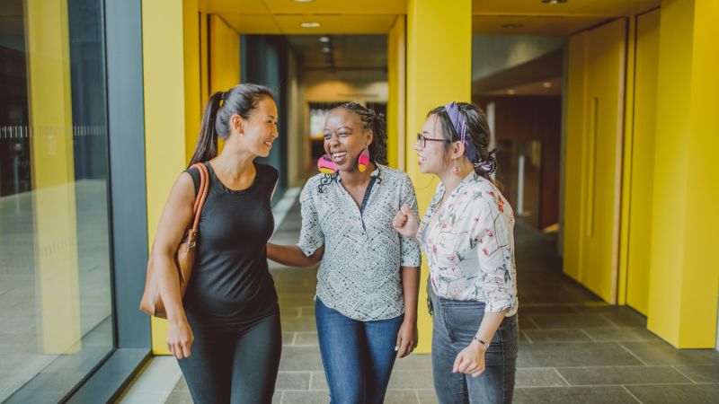 Three students talking to each other in a hallway.