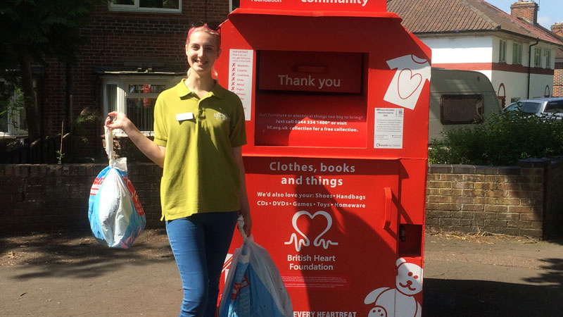 A student ambassador with bags of donated items standing in front of a BHF collection point
