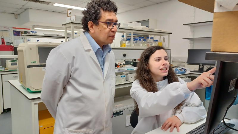 A man and a woman, wearing white laboratory coats looking at a screen