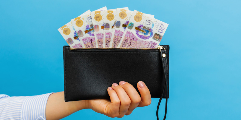 hand holding black wallet showing £20 notes displayed in a fan shape