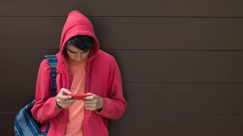 young boy with a pink hoodie on looking at a smartphone