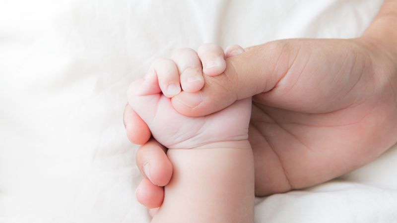 a newborn hand grabbing on to a mother's thumb